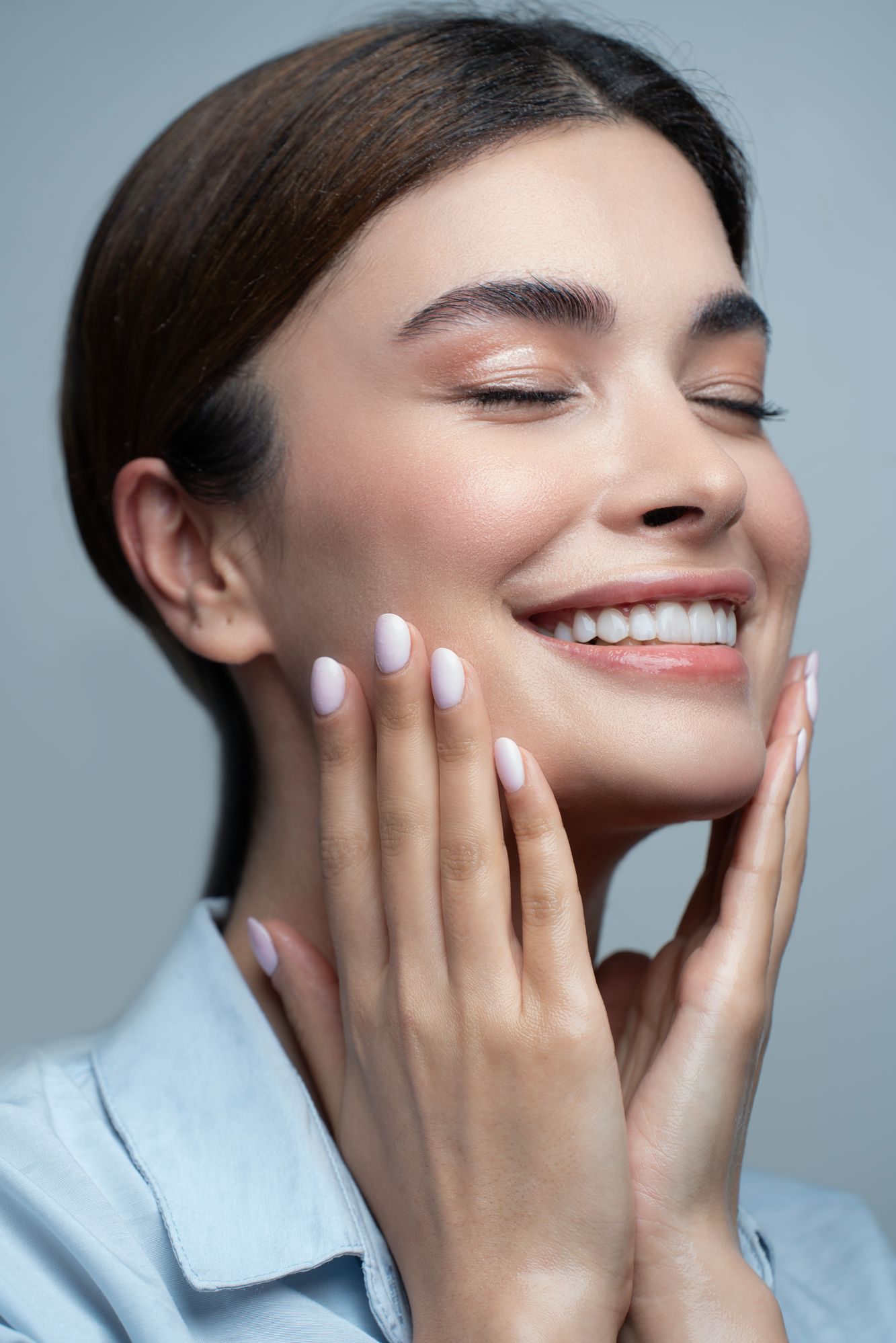 A smiling woman with her eyes closed, hands on her glowing face